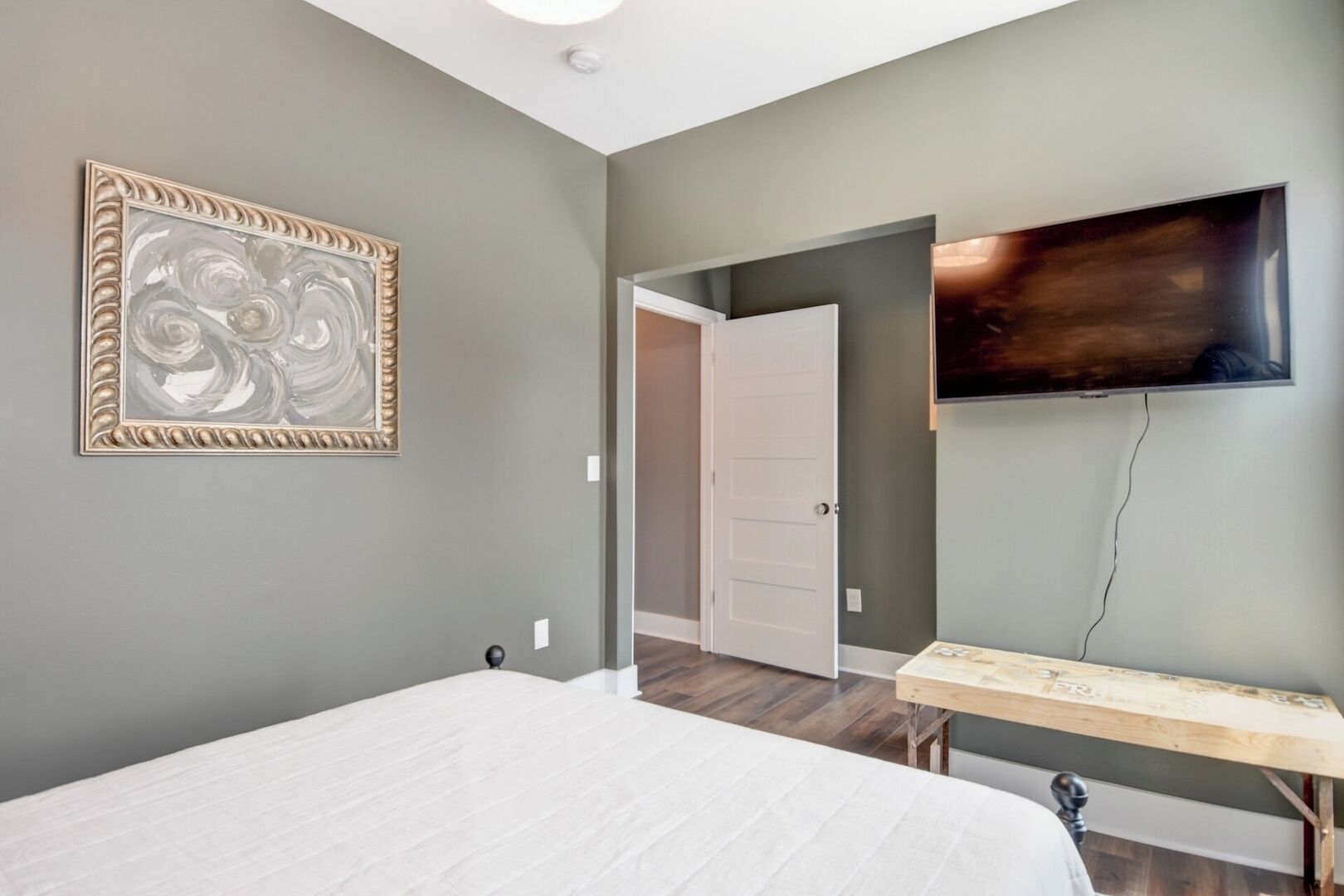A bedroom with a bed, a TV mounted on the wall, and a door leading to another room.