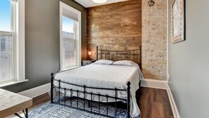 A bedroom with a bed, a window, a wall with a brick pattern, and a hanging light fixture. - Large Milwaukee Home 4BR Fast Wifi (Milwaukee)