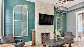 A living room with teal walls, a stone fireplace, a flat-screen TV, and leather furniture. - Large Milwaukee Home 4BR Fast Wifi (Milwaukee)