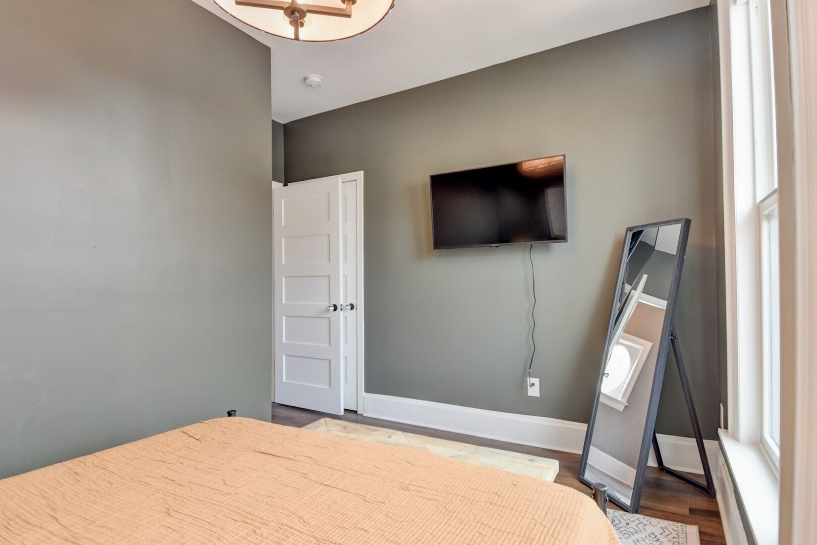 Une chambre à coucher avec un lit, un téléviseur fixé au mur, une porte et une fenêtre.