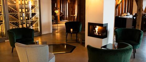 Un interior moderno con una cava de vinos, sillones tapizados en verde, una chimenea y una zona de estar acogedora.