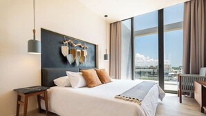 A modern hotel room with a large bed, a view of the city, and a unique wall art piece. - Ocean View • Private Terrace • Luxury Rooftop & 1 Min to Beach (Playa del Carmen)