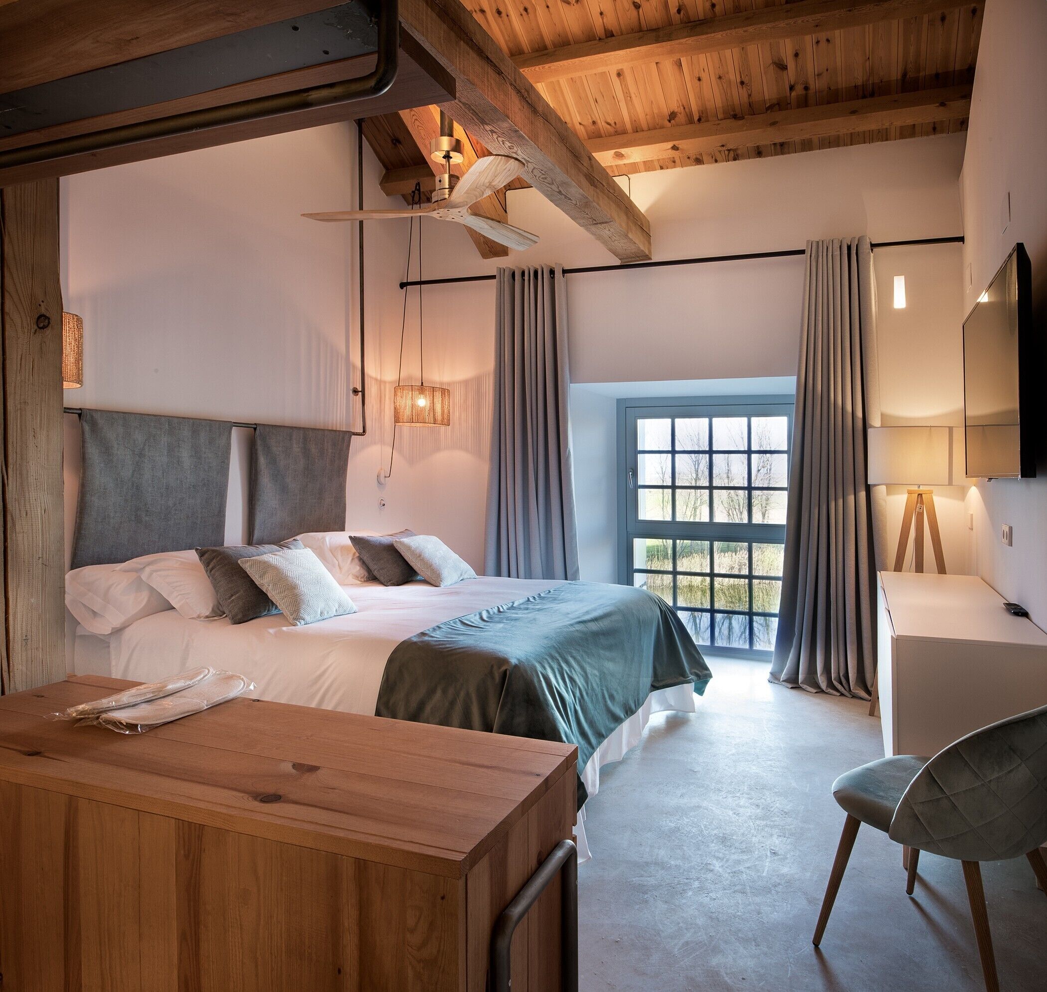 Ein Schlafzimmer mit Bett, Schreibtisch, Stuhl, einem Fenster mit Vorhängen und Deckenventilator.