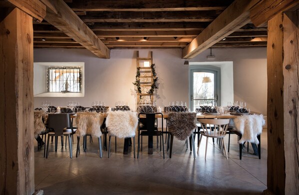 A dining area with wooden beams, a ladder with greenery, and fur-covered chairs.