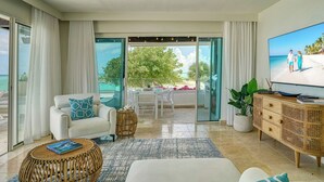 En moderne stue med en hvid sofa, et fletbord, et fladskærms-tv og en balkon med udsigt over stranden.