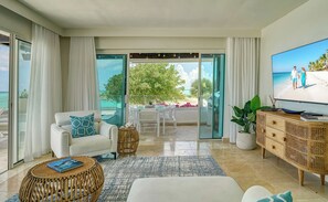 Ein modernes Wohnzimmer mit einem weißen Sofa, einem Korbtisch, einem Flachbildfernseher und einem Balkon mit Blick auf den Strand.