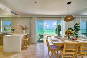 Eine moderne Küche mit einer großen Kochinsel, einem Essbereich mit Holzsesseln und Blick aufs Meer.