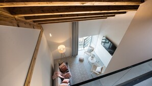 A modern interior with a staircase, a sofa with cushions, a lamp, and a dining area with chairs and a table.