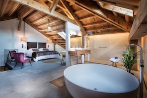 A bedroom with a large bed, a sitting area with a chair, a large bathtub, and a wooden ceiling structure. - Luxury Suite Magia de las Estrellas in Palencia, with Wi-Fi (Abarca de Campos)