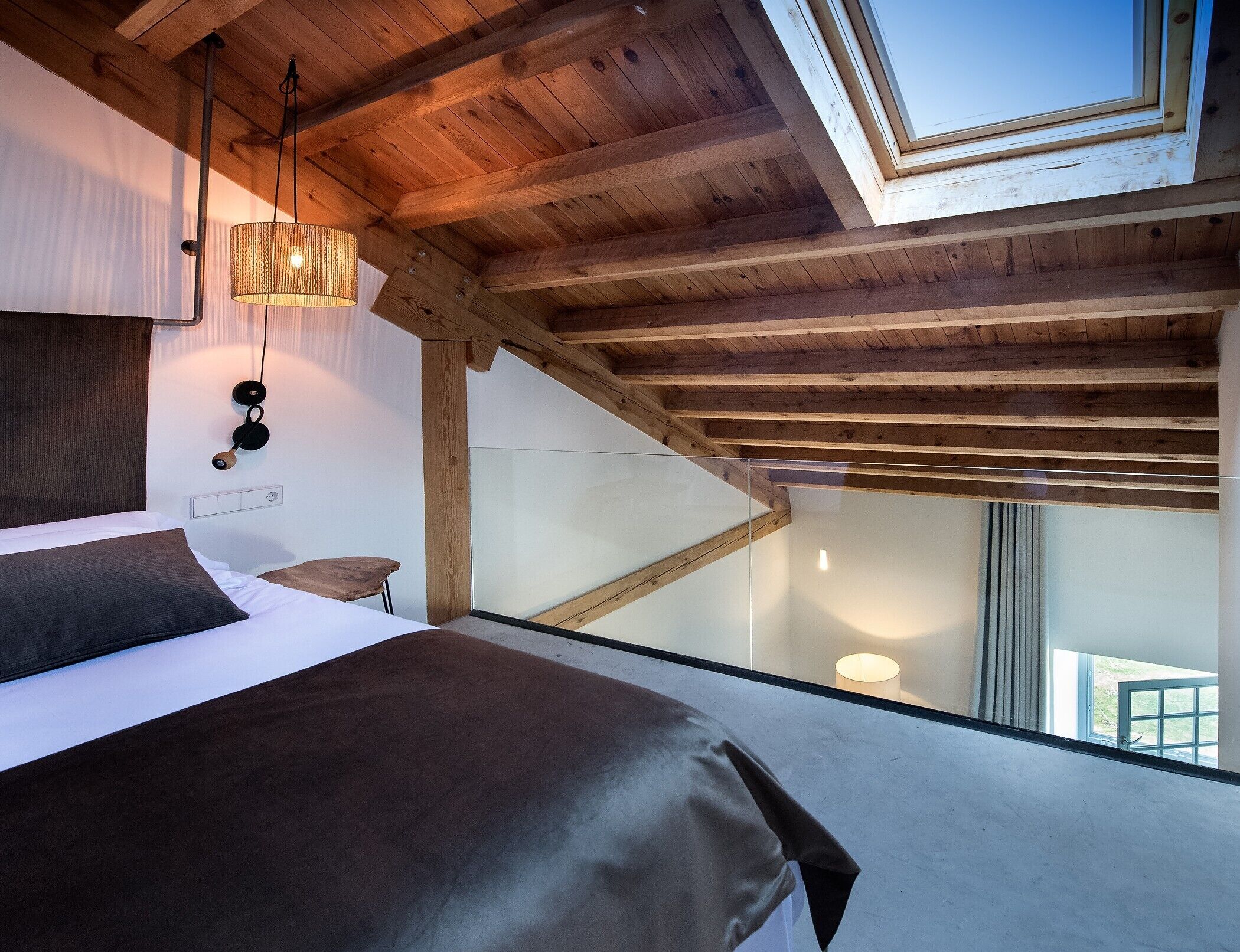 Un dormitorio con cama, lámpara colgante, techo de madera y tragaluz.