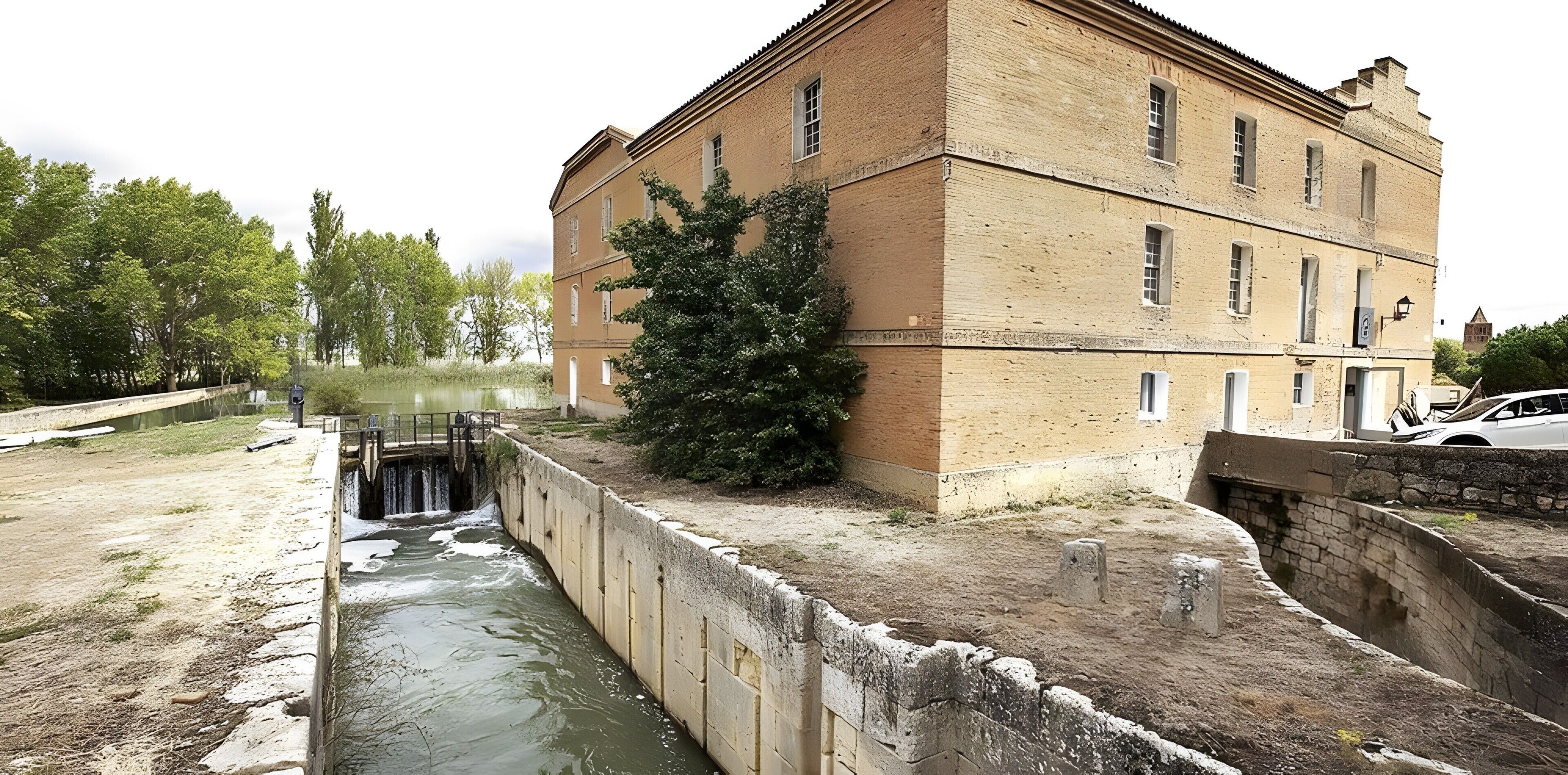 A brick building with a water channel, a tree, and a stone wall.