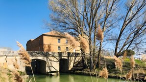 Un edificio con un puente sobre un río, rodeado de árboles y vegetación.