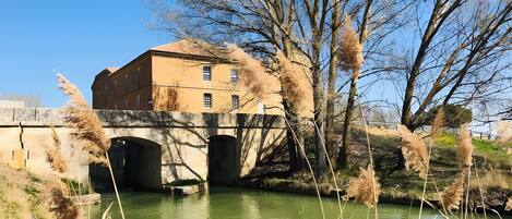 A building with a bridge over a river, surrounded by trees and vegetation.