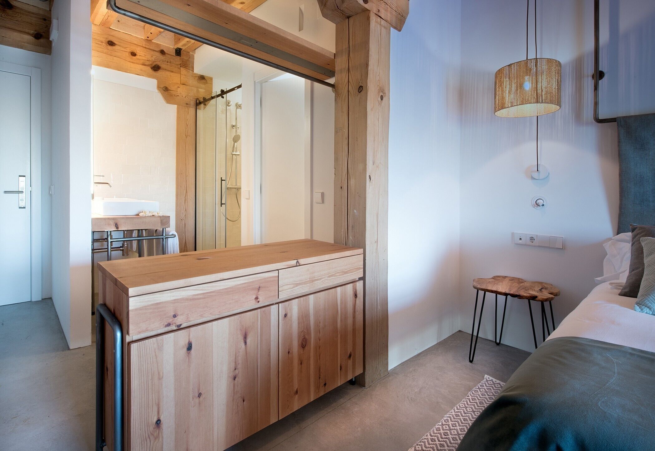 Un baño moderno con un tocador de madera, un espejo, una ducha y una lámpara colgante.