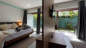 Ett modernt hotellrum med en säng, ett nattduksbord och utsikt över den utomhusliggande trädgården.