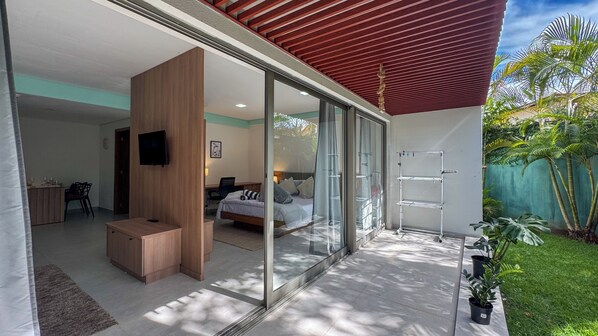 Una habitación de hotel moderna con puerta de vidrio que da a un balcón, una cama, un escritorio y un televisor.