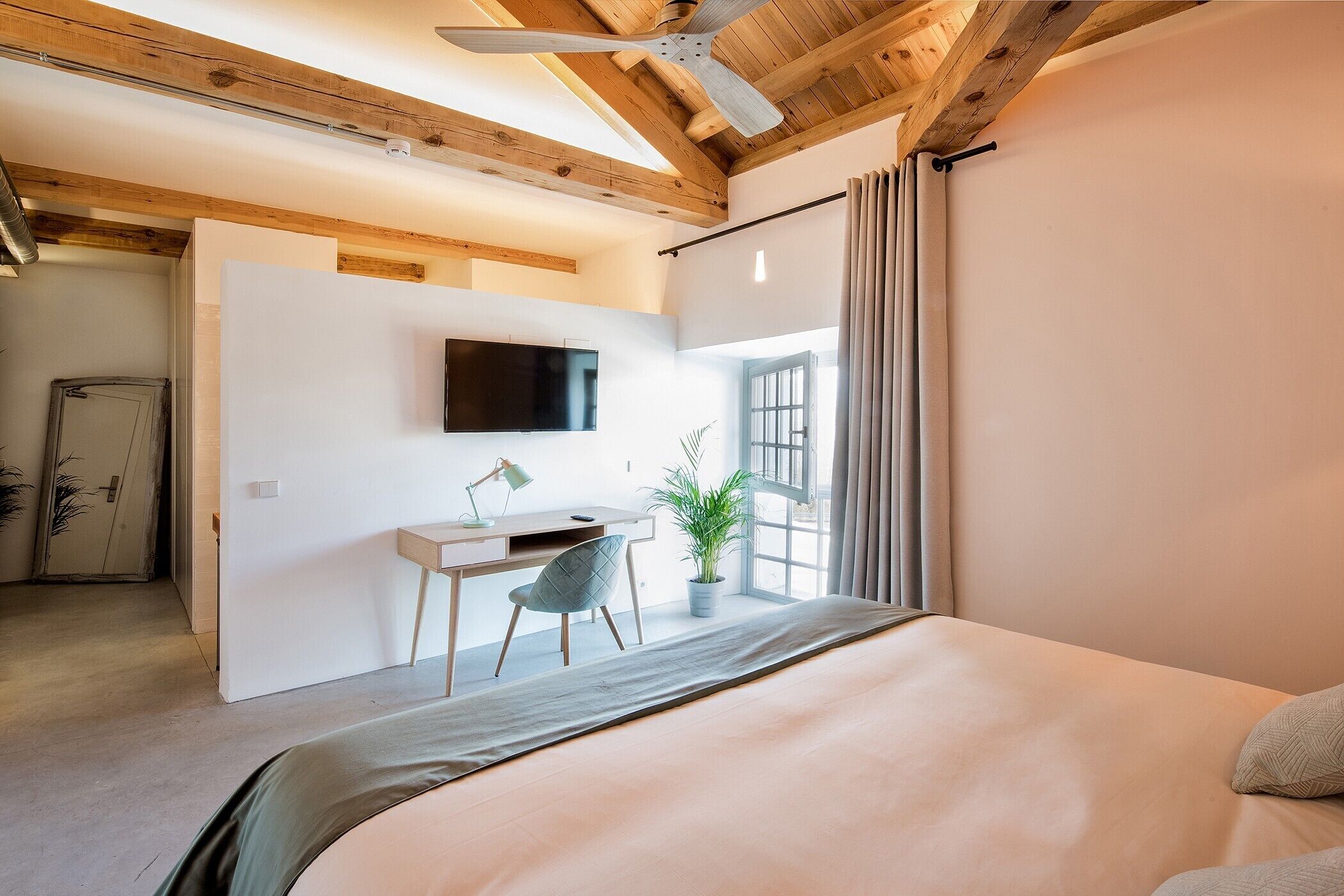 A bedroom with a bed, desk, chair, and a TV mounted on the wall.