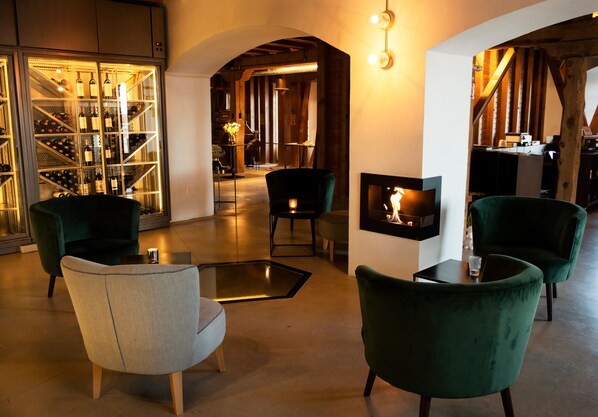 A modern interior with a wine cellar, green upholstered chairs, a fireplace, and a cozy seating area.