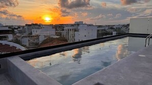 Ein Pool auf dem Dach mit Blick auf den Sonnenuntergang, umgeben von modernen Gebäuden.