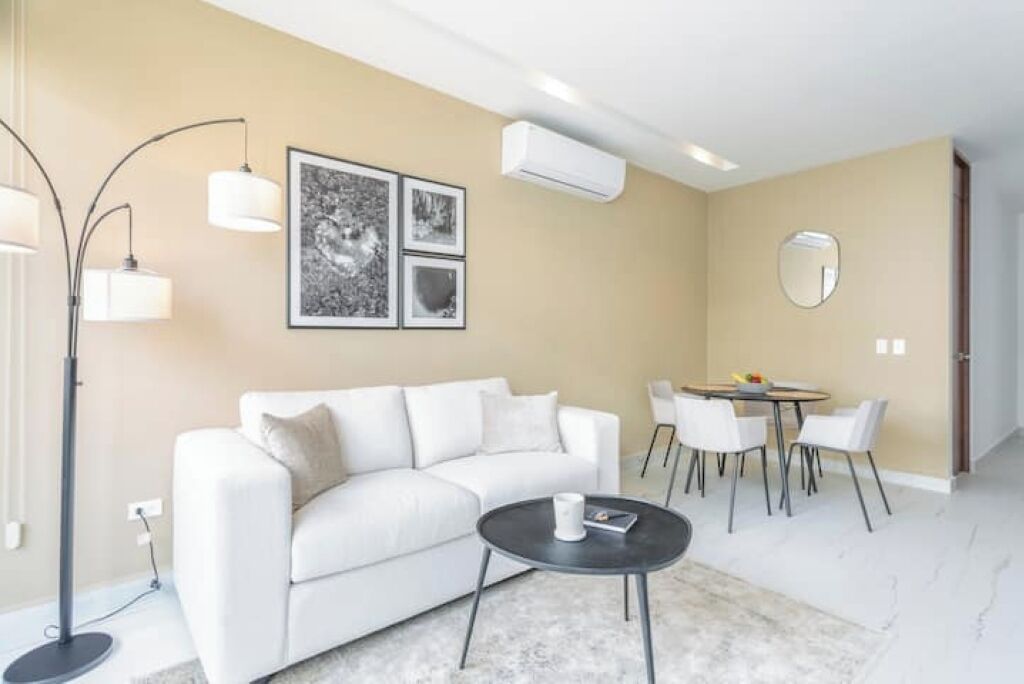 Een moderne woonkamer met een witte bank, een ronde salontafel en een eethoek met een kleine tafel en stoelen.