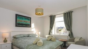 A neatly arranged bedroom with a bed, bedside tables, a chair, and a window with curtains. - 32A Bank Street (Rossendale)
