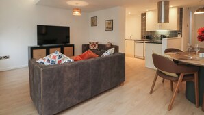 A modern living room with a grey sofa, a flat-screen TV, and a dining area with a table and chairs. - 32A Bank Street (Rossendale)