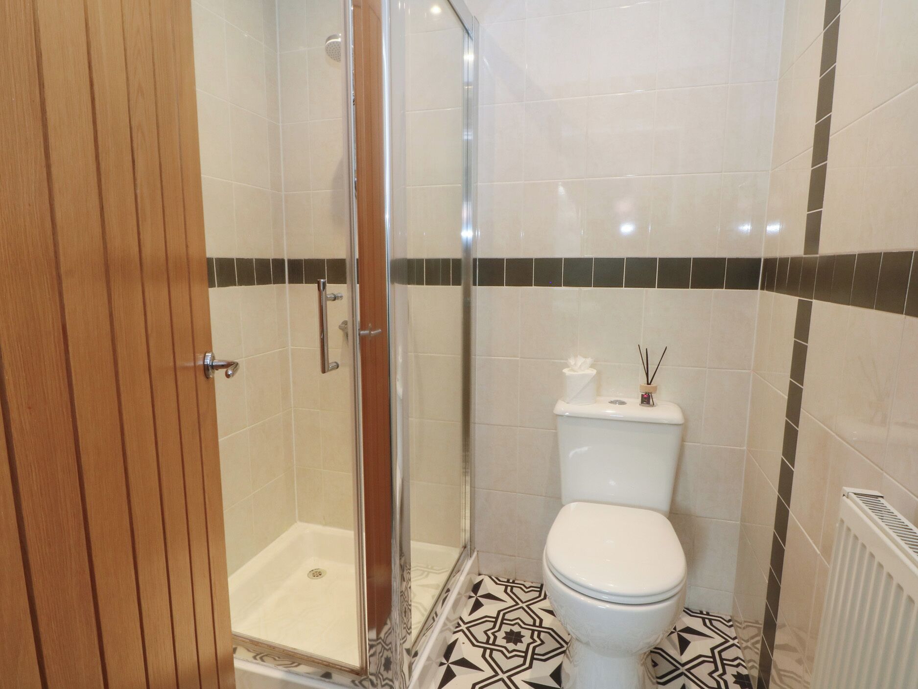 A bathroom with a shower, toilet, and a patterned floor.