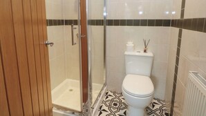 A bathroom with a shower, toilet, and a patterned floor. - 32A Bank Street (Rossendale)