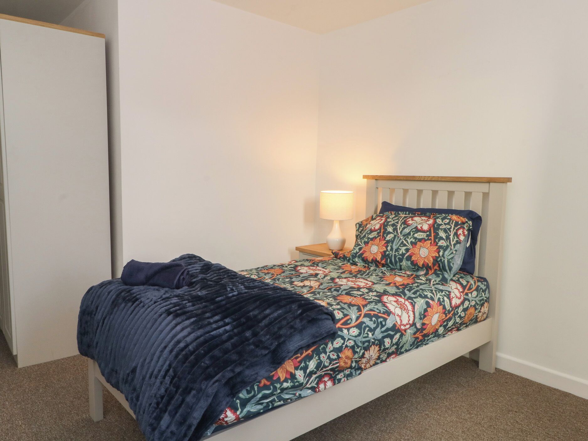A single bed with a floral-patterned bedspread, a dark blue blanket, and a wooden headboard.