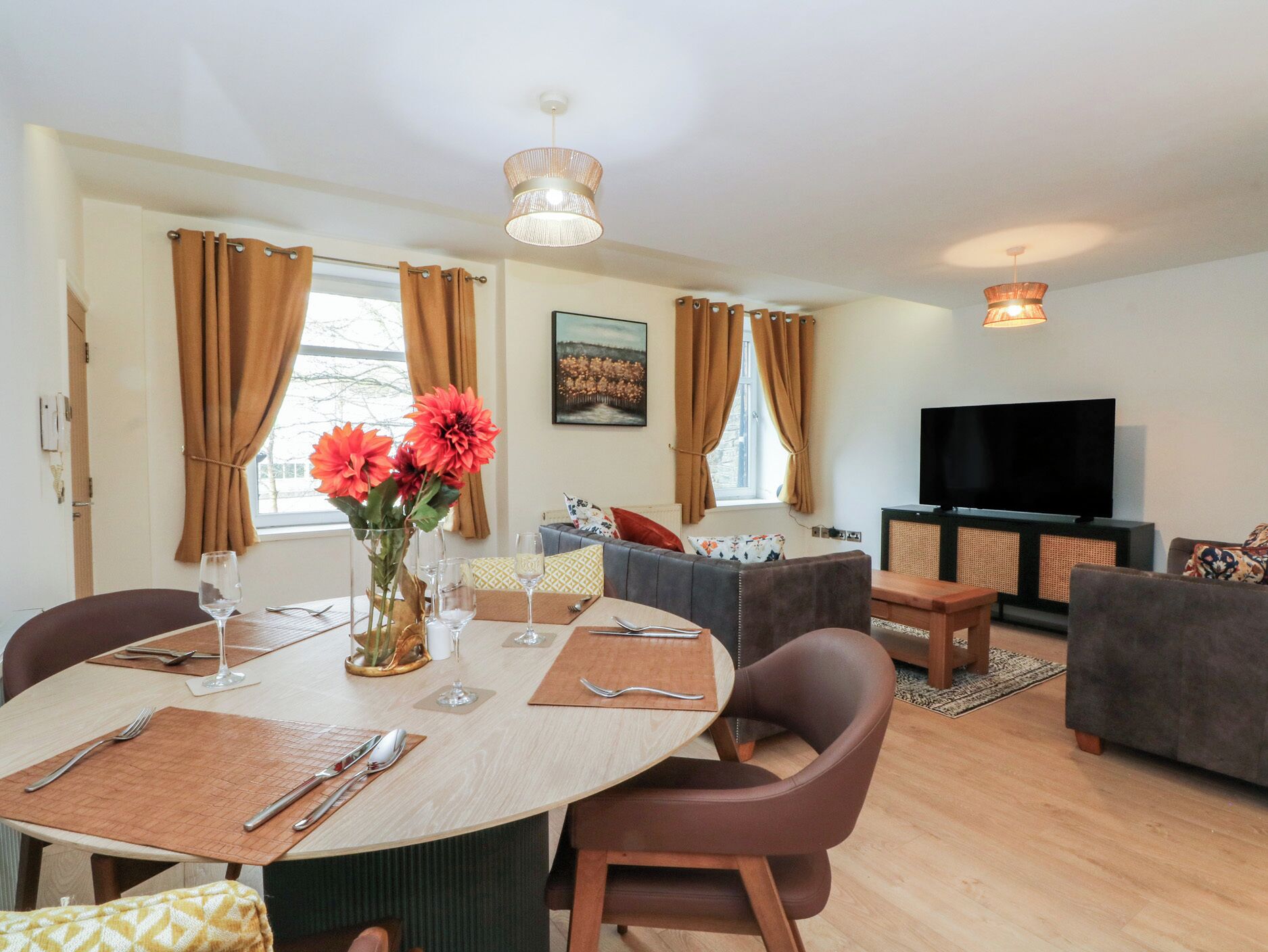 A modern living room with a dining area, a flat-screen TV, and a large window with curtains.