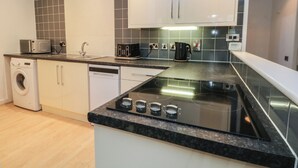 A modern kitchen with a built-in washing machine, a microwave, a toaster, and a coffee maker. - 32A Bank Street (Rossendale)