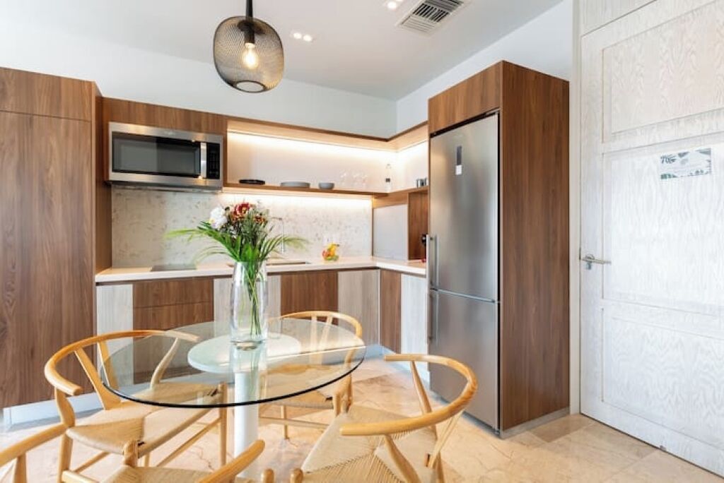 Una cocina moderna con armarios de madera, electrodomésticos de acero inoxidable y una mesa de comedor de vidrio con sillas de mimbre.