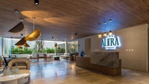 Un hall d’hôtel moderne avec un plafond en bois, un comptoir d’accueil et une vue sur la verdure environnante.