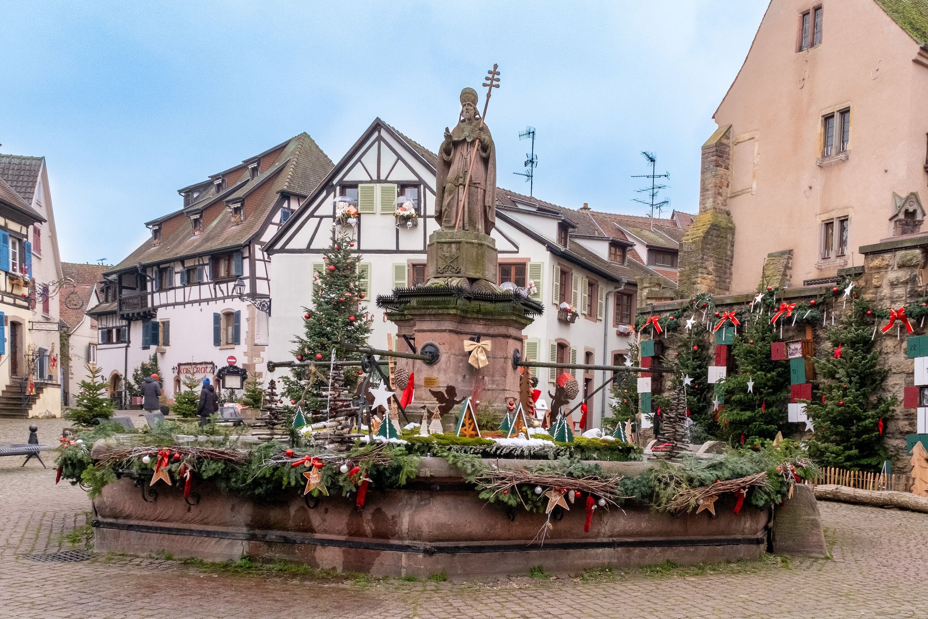 A traditional European town square with a central fountain, surrounded by historic buildings and festive Christmas decorations.