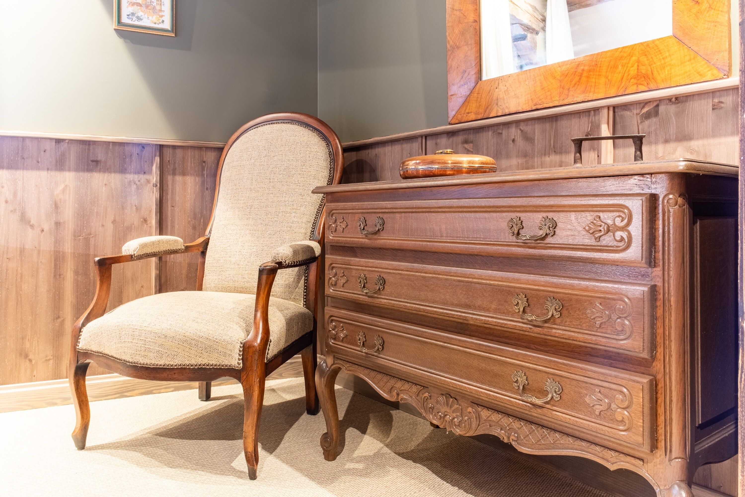 Une commode en bois ornée de sculptures complexes et un fauteuil rembourré avec un siège en osier tressé.