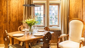 A wooden dining table with chairs, a vase with flowers, and a window with curtains. - Appartement Château Pape - A quelques minutes de Colmar (Eguisheim)
