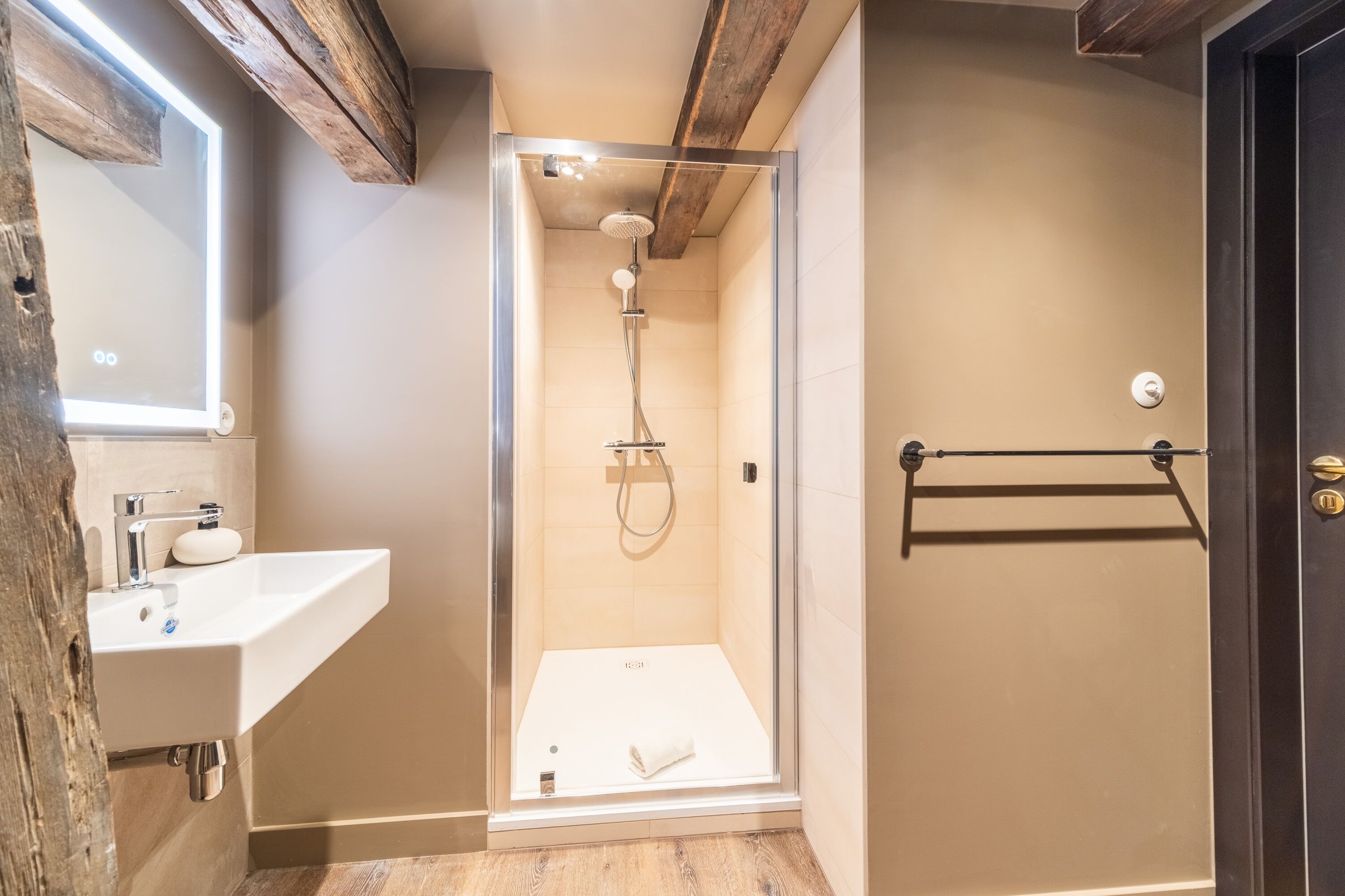 Ein modernes Badezimmer mit einer gläsernen Duschkabine, einem weißen Waschbecken und einem Holzbalken an der Decke.