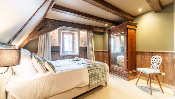 A bedroom with a large bed, wooden beams, a mirror, and a window with curtains. - Appartement Château Pape - A quelques minutes de Colmar (Eguisheim)