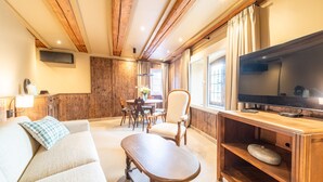 A cozy living room with a wooden ceiling, a flat-screen TV, a sofa, a coffee table, and a dining area with a table and chairs. - Appartement Château Pape - A quelques minutes de Colmar (Eguisheim)
