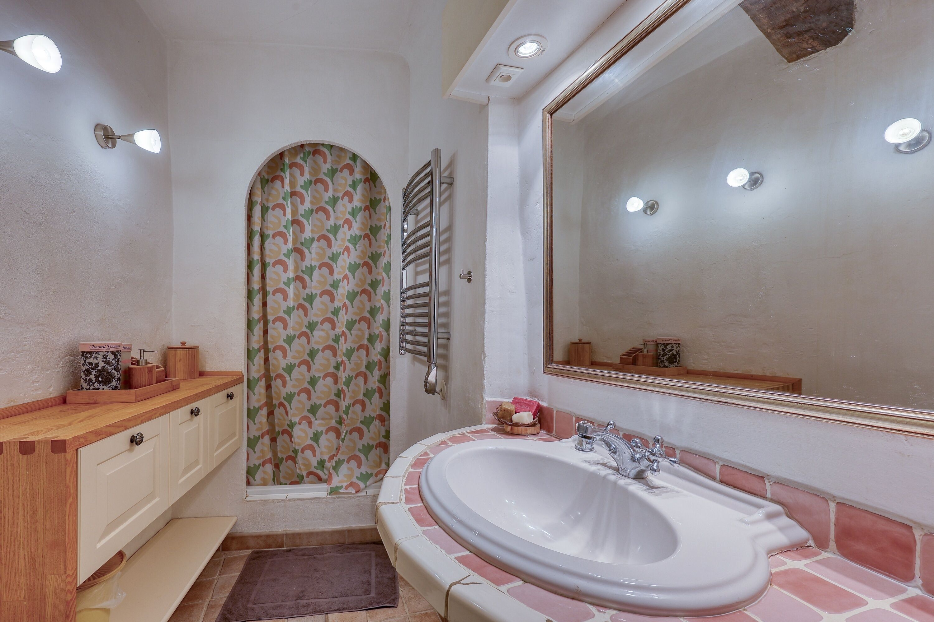 Ein Badezimmer mit einem weißen Waschbecken, einem Spiegel und einer Dusche mit einem blumigen Vorhang.