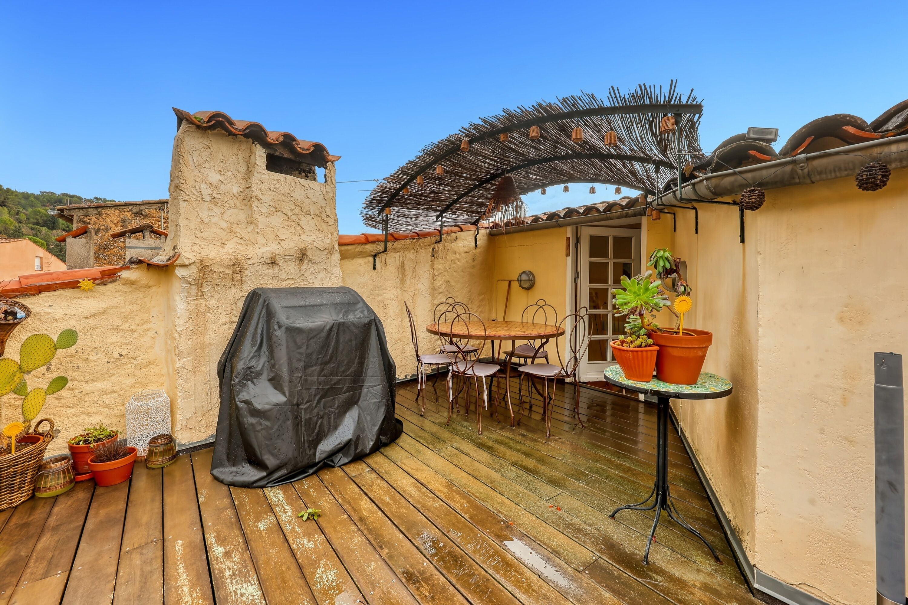 A patio with a covered grill, a table with chairs, and potted plants.
