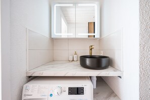 Ein Badezimmer mit Marmorplatte, einem schwarzen Waschbecken, einem Spiegel und einer Dampfduschsteuerung.