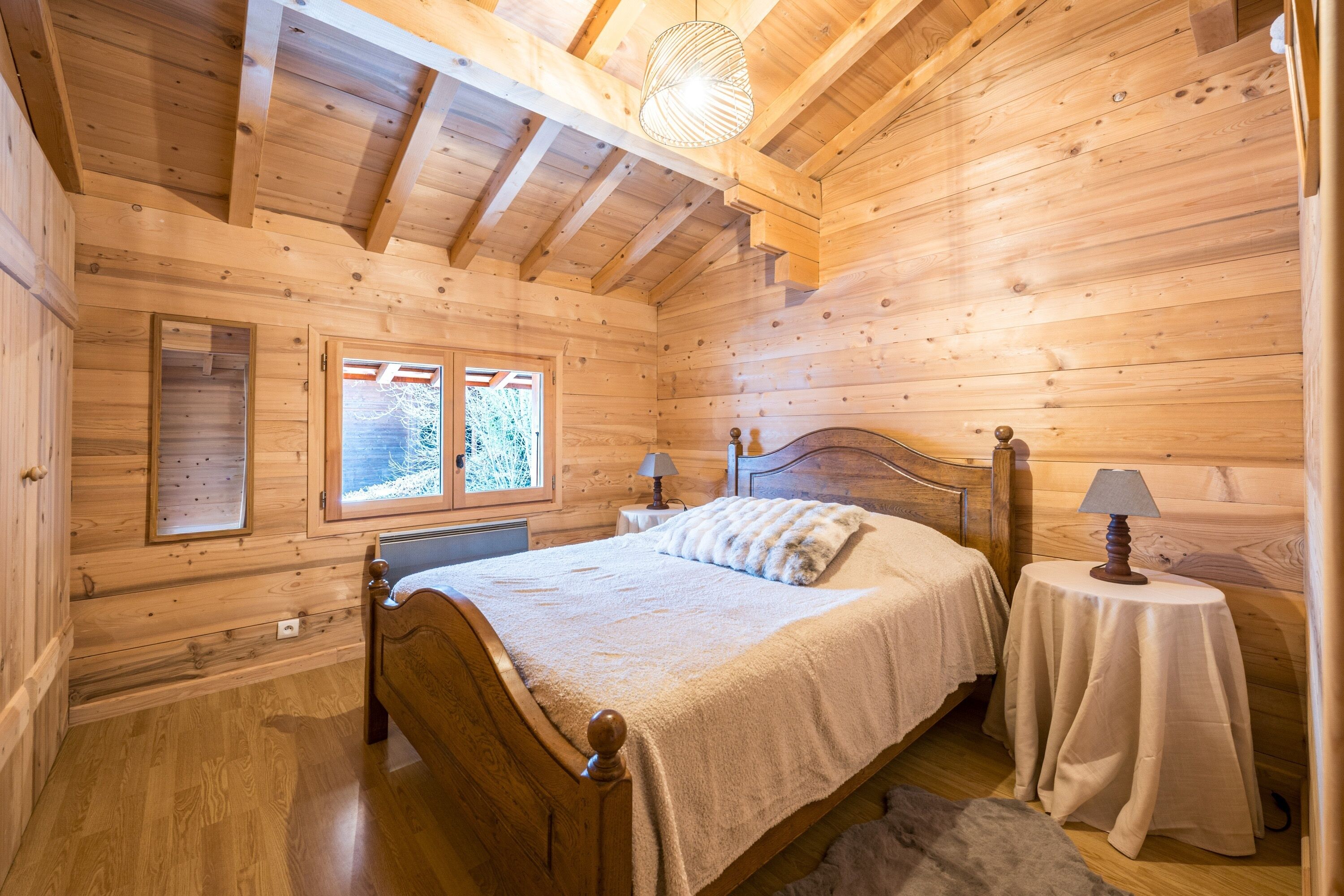 Une chambre à coucher située dans une cabane en bois, avec un lit, deux tables de chevet, une fenêtre et un luminaire au plafond.
