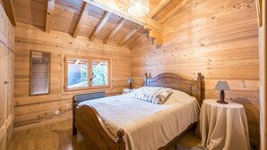 Ein Schlafzimmer einer Holzhütte mit einem Bett, zwei Nachttischen, einem Fenster und einer Deckenleuchte.