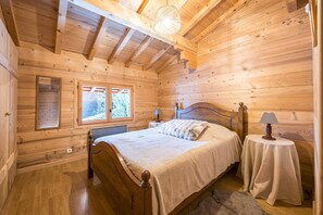 Une chambre à coucher située dans une cabane en bois, avec un lit, deux tables de chevet, une fenêtre et un luminaire au plafond.