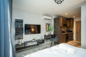 Een moderne hotelkamer met een groot bed, een aan de muur bevestigde televisie, een zithoekje en een kitchenette.