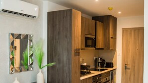 A compact kitchen with wooden cabinets, a microwave, and a coffee maker. - Serene New Studio Apartment @ The Bantree (Accra)