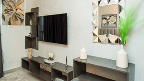 A modern living room with a flat-screen TV, a large mirror, and a grey sofa. - Serene New Studio Apartment @ The Bantree (Accra)