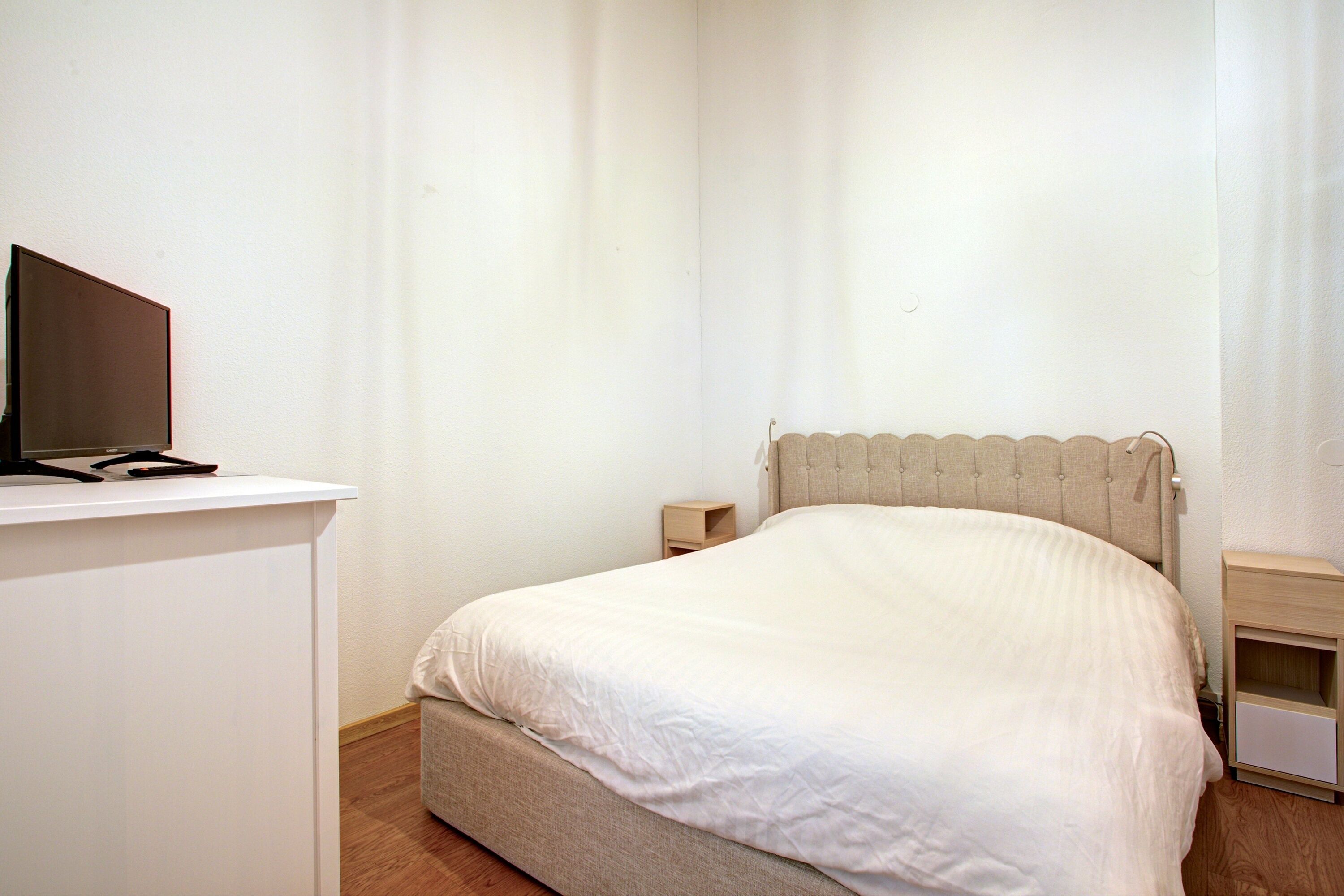 A bedroom with a bed, a bedside table, a nightstand, and a desk with a chair.