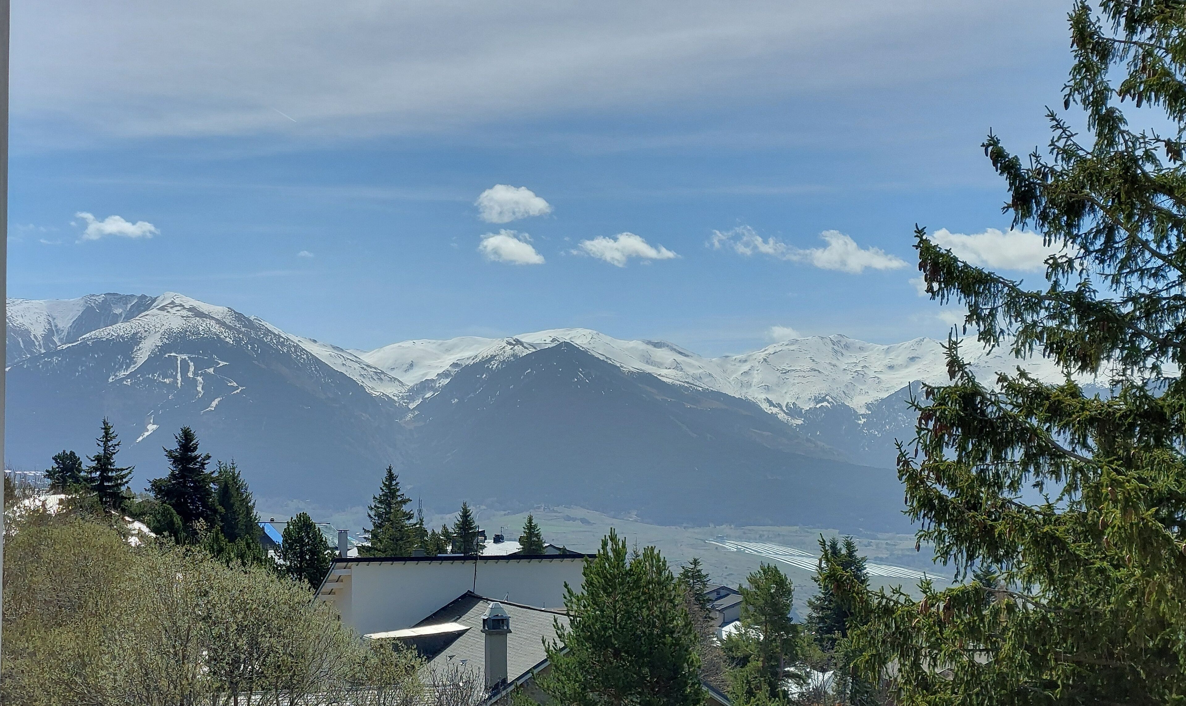 A mountain landscape with snow-capped peaks, a clear sky, and a view of a valley below.
